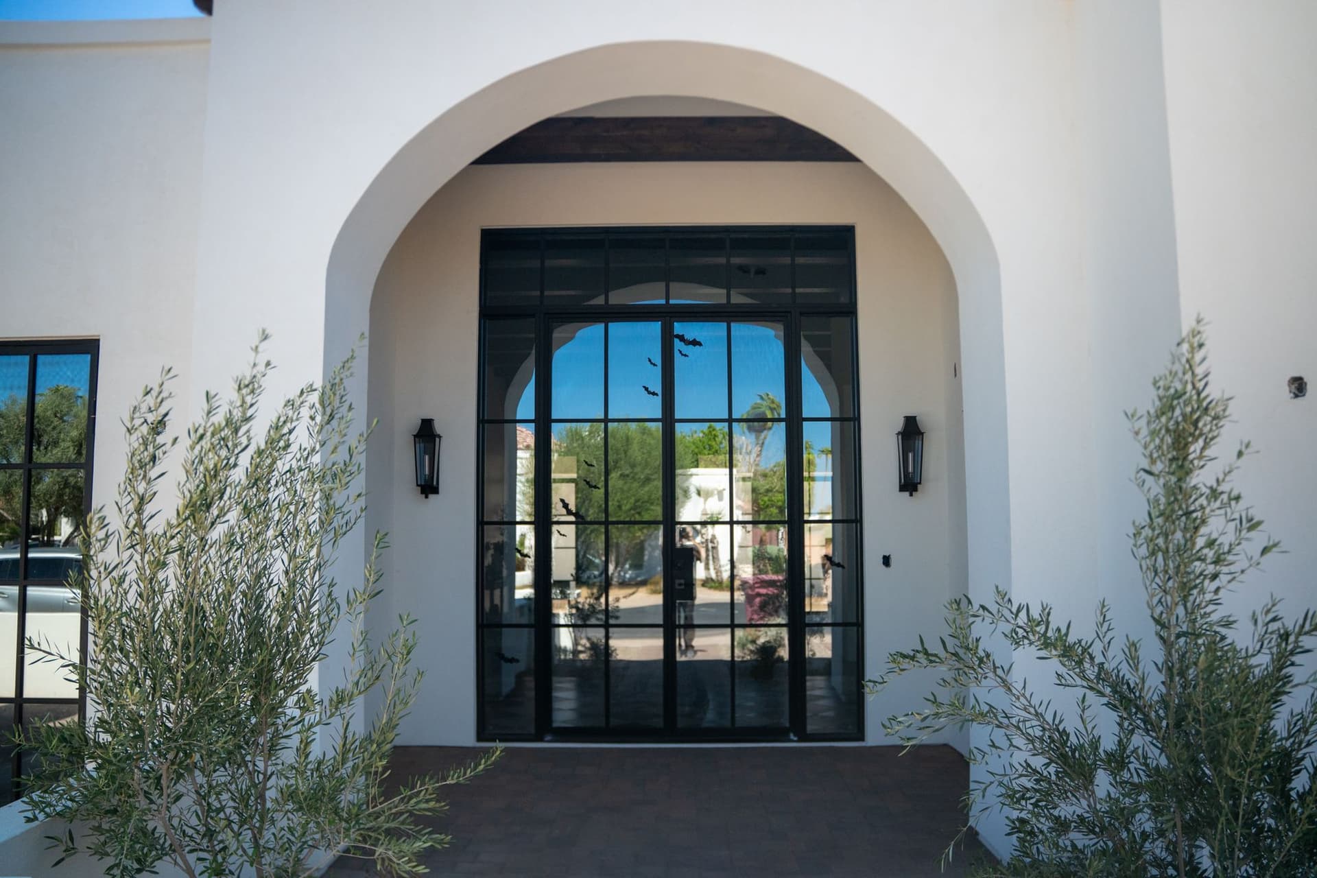 Completed home's arched white stucco entrance with a black metal and glass door